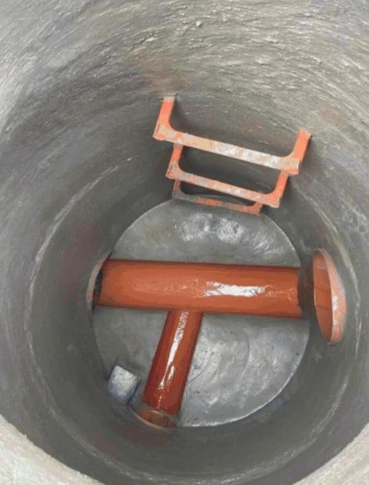 Interior de pozo con conexiones de tubería naranja en T y pates de acceso